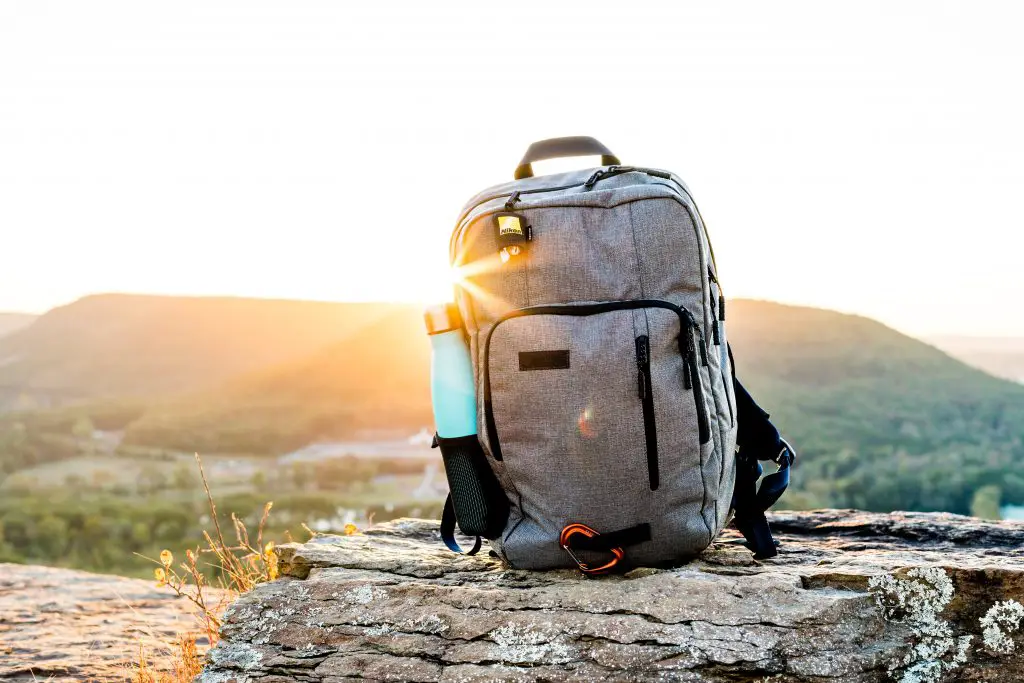 grey and black hiking backpack and cyan tumbler on grey rock during sunset